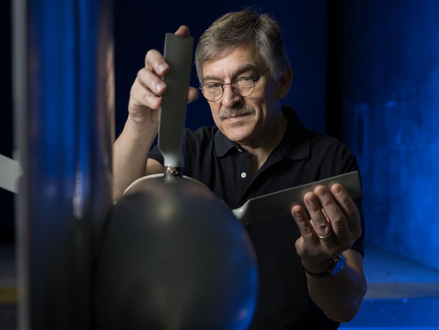 A researcher holding a small dark aerodynamic model, lit against a blue background.