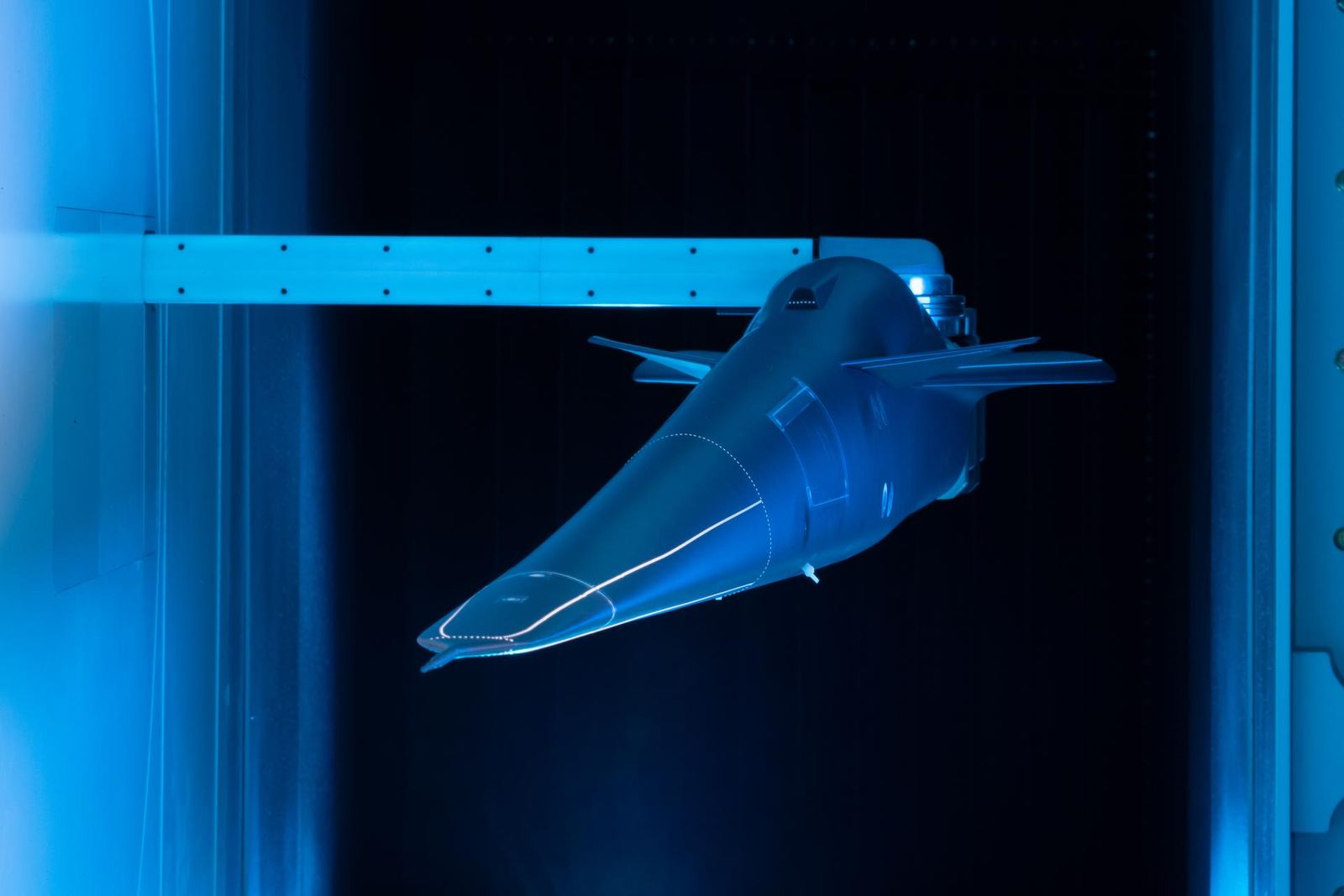A scale model of the X-59 supersonic research aircraft in a wind tunnel, lit blue against a dark background.